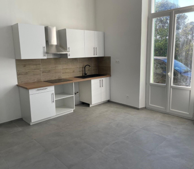 Une petite cuisine moderne et minimaliste avec des meubles blancs, un plan de travail en bois et un sol carrelé gris.