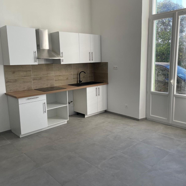 Une petite cuisine moderne et minimaliste avec des meubles blancs, un plan de travail en bois et un sol carrelé gris.