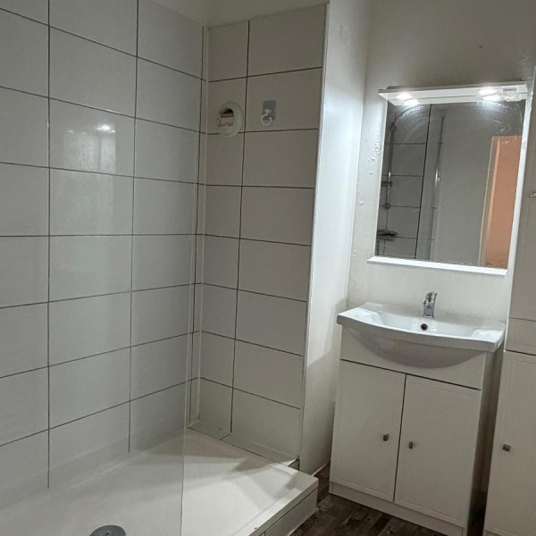 Salle de bain simple avec douche, lavabo et miroir, décorée en blanc.