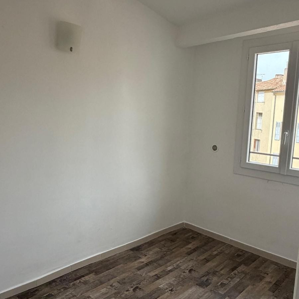 Une pièce lumineuse et simple, avec un sol en bois et une fenêtre ouverte.