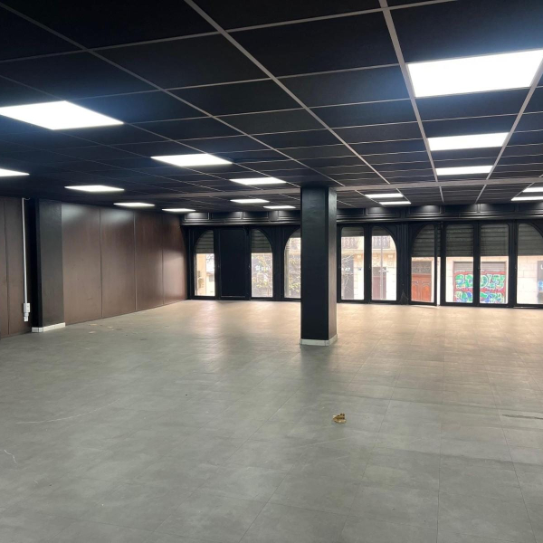 Un grand local commercial vide avec un plafond noir et des dalles d'éclairage carrées.