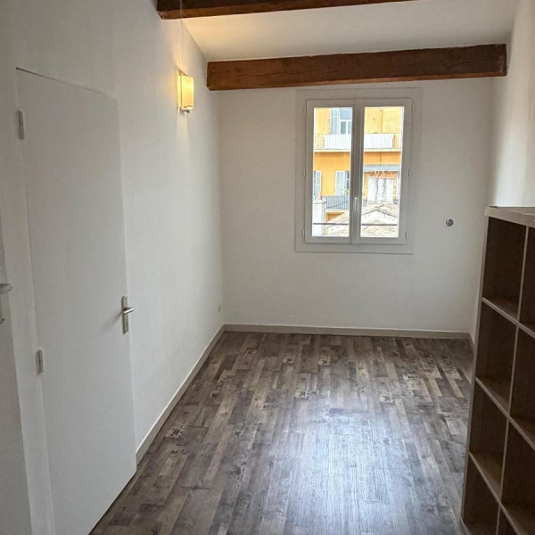 Pièce lumineuse et simple avec un sol en bois et une fenêtre.