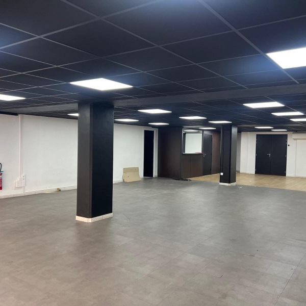 Intérieur d'un local commercial vide avec un plafond noir, des dalles de sol grises et des murs blancs.