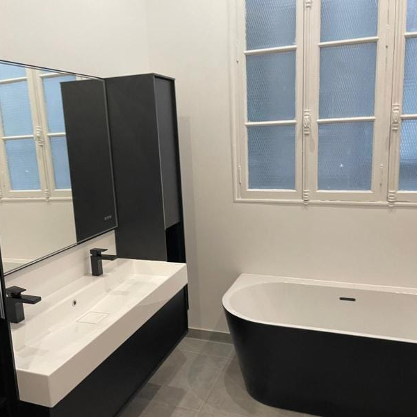 Salle de bain moderne avec baignoire autoportante, lavabo et armoire noire.
