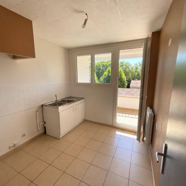 Une petite cuisine vide avec un évier blanc, un sol carrelé et une porte-fenêtre ouverte sur l'extérieur.