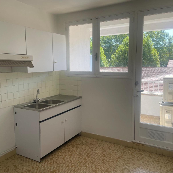 Cuisine blanche minimaliste avec un évier double en inox et une porte-fenêtre donnant sur un balcon.