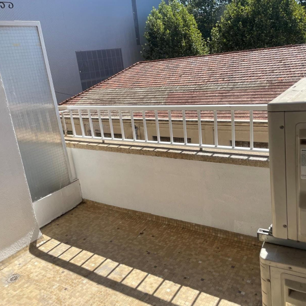 Vue d'un petit balcon carrelé avec une rambarde blanche et un climatiseur extérieur.