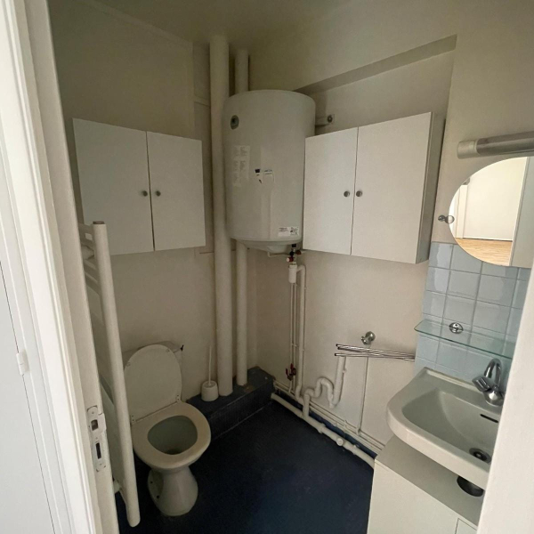 Intérieur d'une petite salle de bain blanche avec un lavabo, des toilettes et un chauffe-eau électrique.