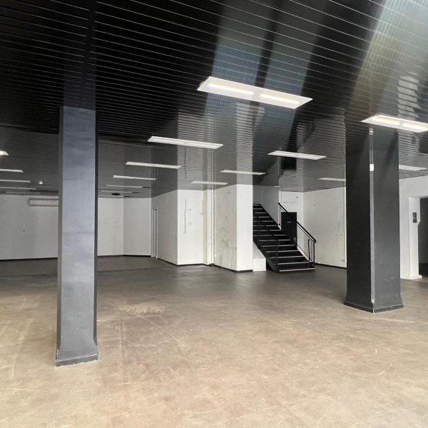 Intérieur d'un grand espace vide et moderne avec un plafond noir à lattes, des piliers noirs et un escalier noir.