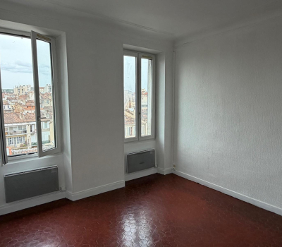 Pièce lumineuse et neutre avec deux fenêtres donnant sur la ville.