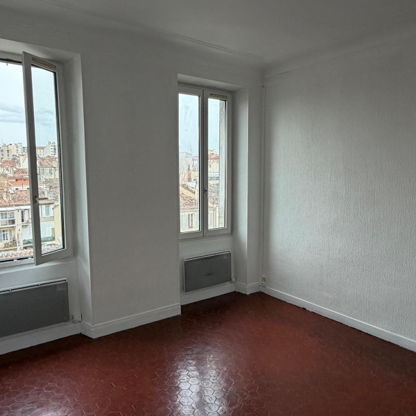 Pièce lumineuse et neutre avec deux fenêtres donnant sur la ville.