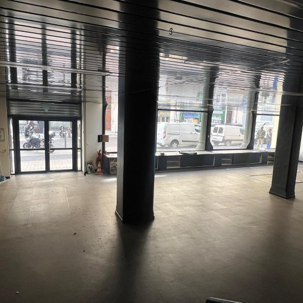 Intérieur d'un local commercial vide avec un plafond métallique et de grandes baies vitrées donnant sur la rue.