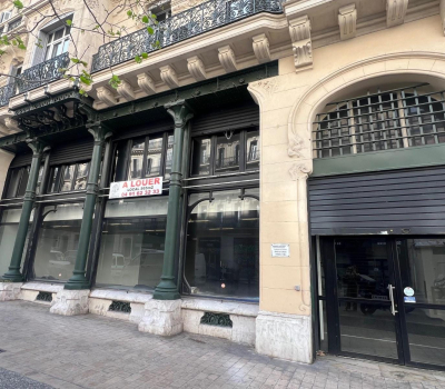 Façade d'un immeuble haussmannien avec un local commercial à louer et des colonnes en fer forgé vert.