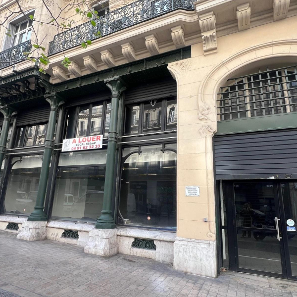 Façade d'un immeuble haussmannien avec un local commercial à louer et des colonnes en fer forgé vert.