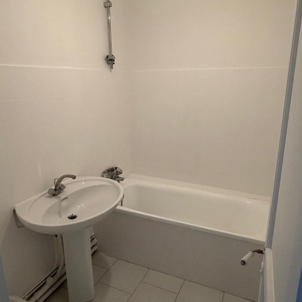 Salle de bain simple et épurée avec baignoire, lavabo et murs blancs.