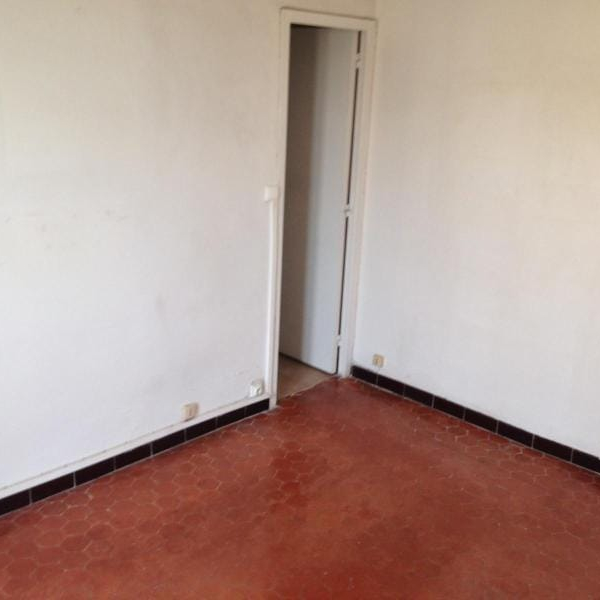 Une pièce vide avec des murs blancs, un sol en carrelage rouge et une porte ouverte.