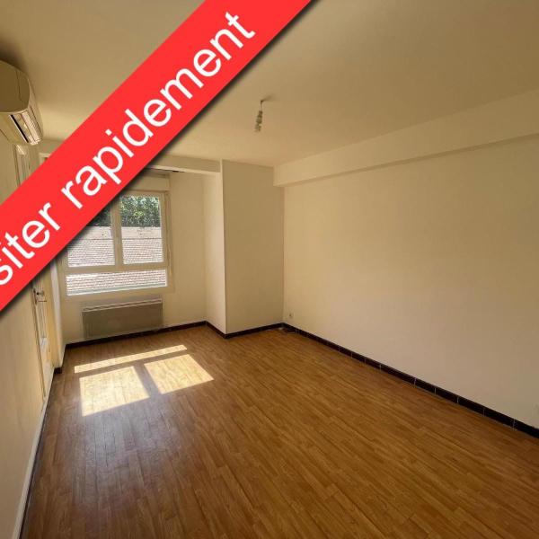 Une pièce vide avec un parquet en bois, des murs blancs et une fenêtre laissant entrer la lumière du soleil.